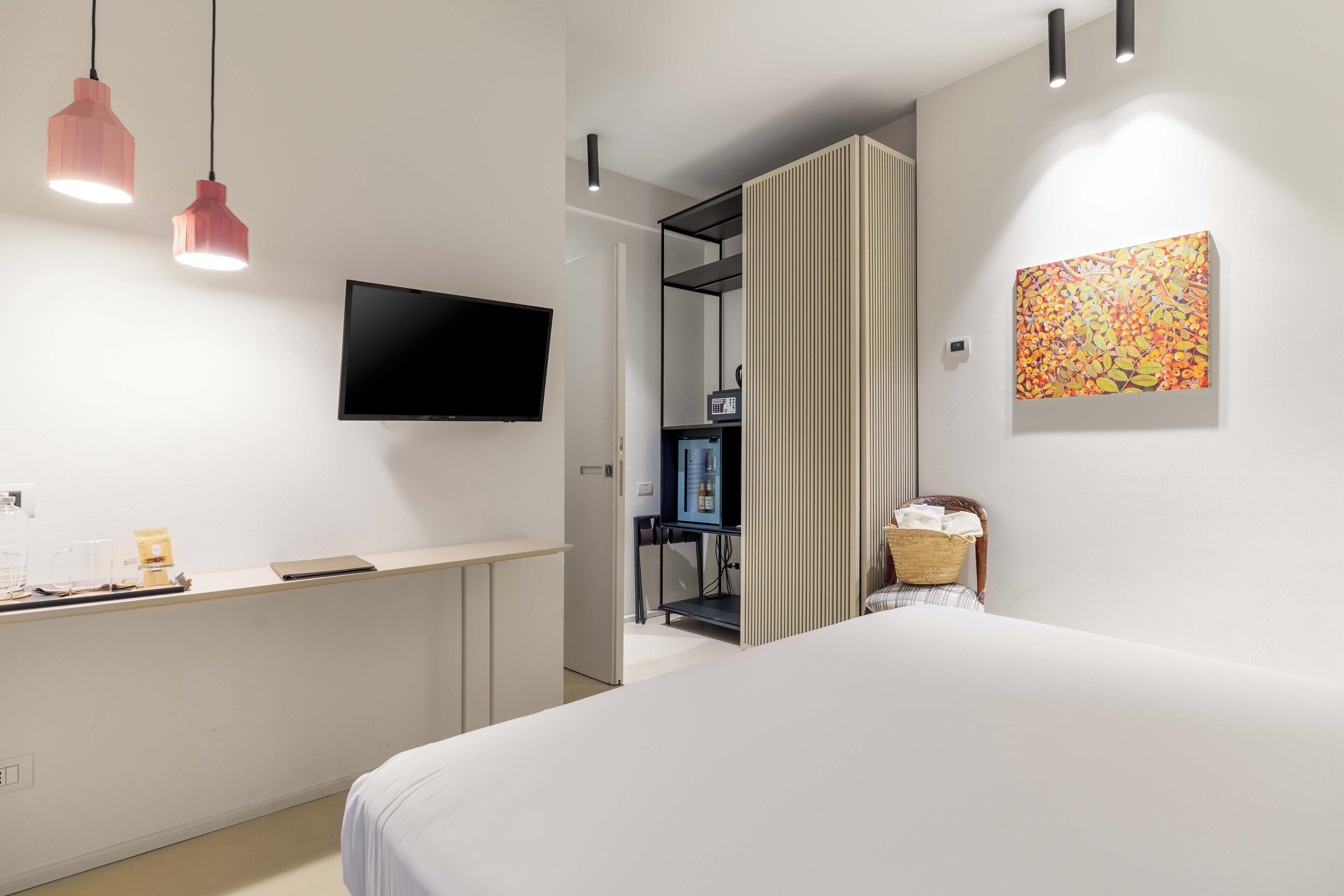 Hotellihuone, jossa on sänky, seinälle asennettu televisio, työpöytä, jossa on kahvinkeitin, ja seinällä taulu.