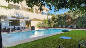 Una piscina al aire libre, sombrillas, sillones reclinables de piscina