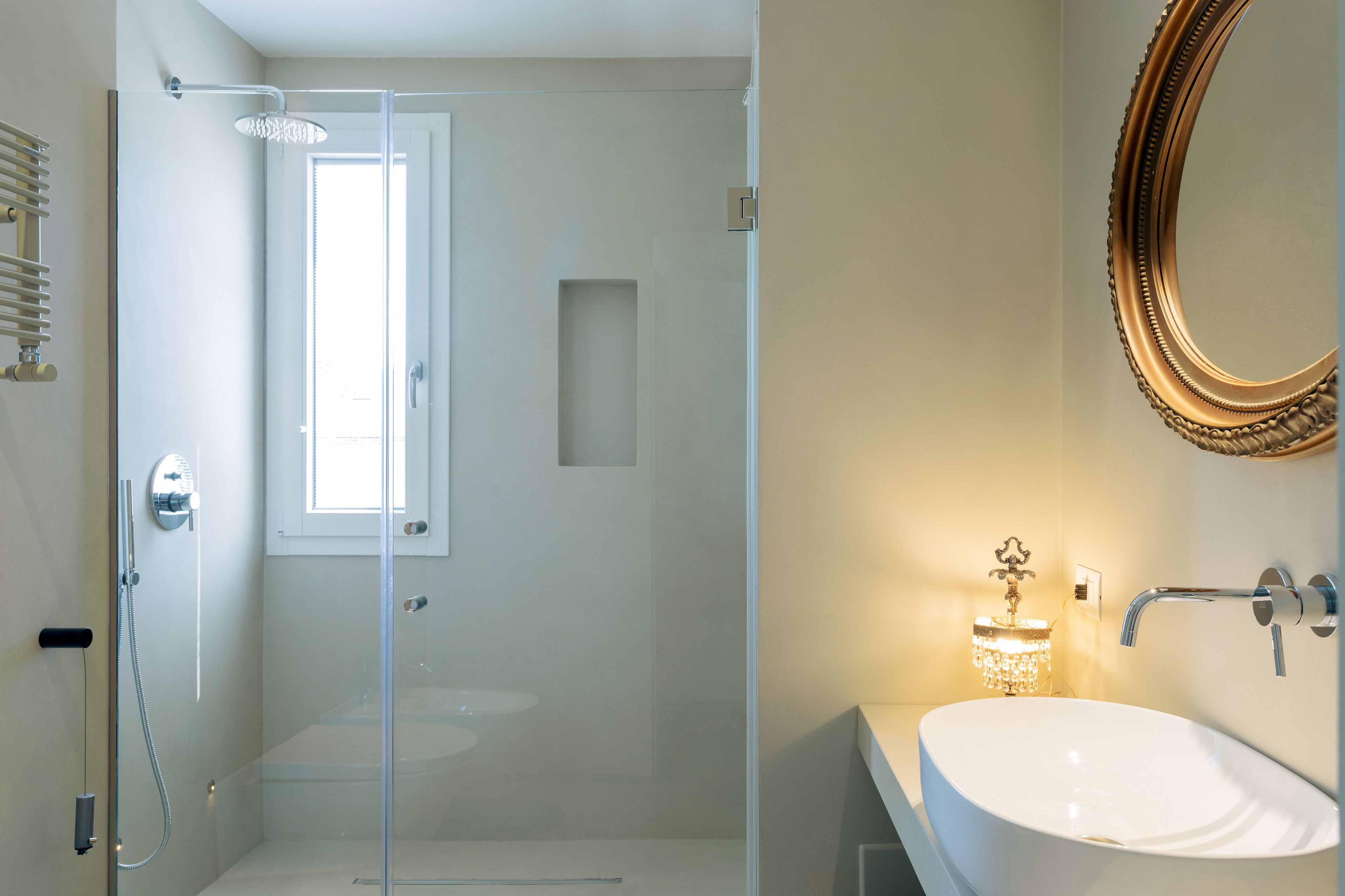 Un baño moderno con ducha de vidrio, lavamanos blanco y un espejo decorativo.