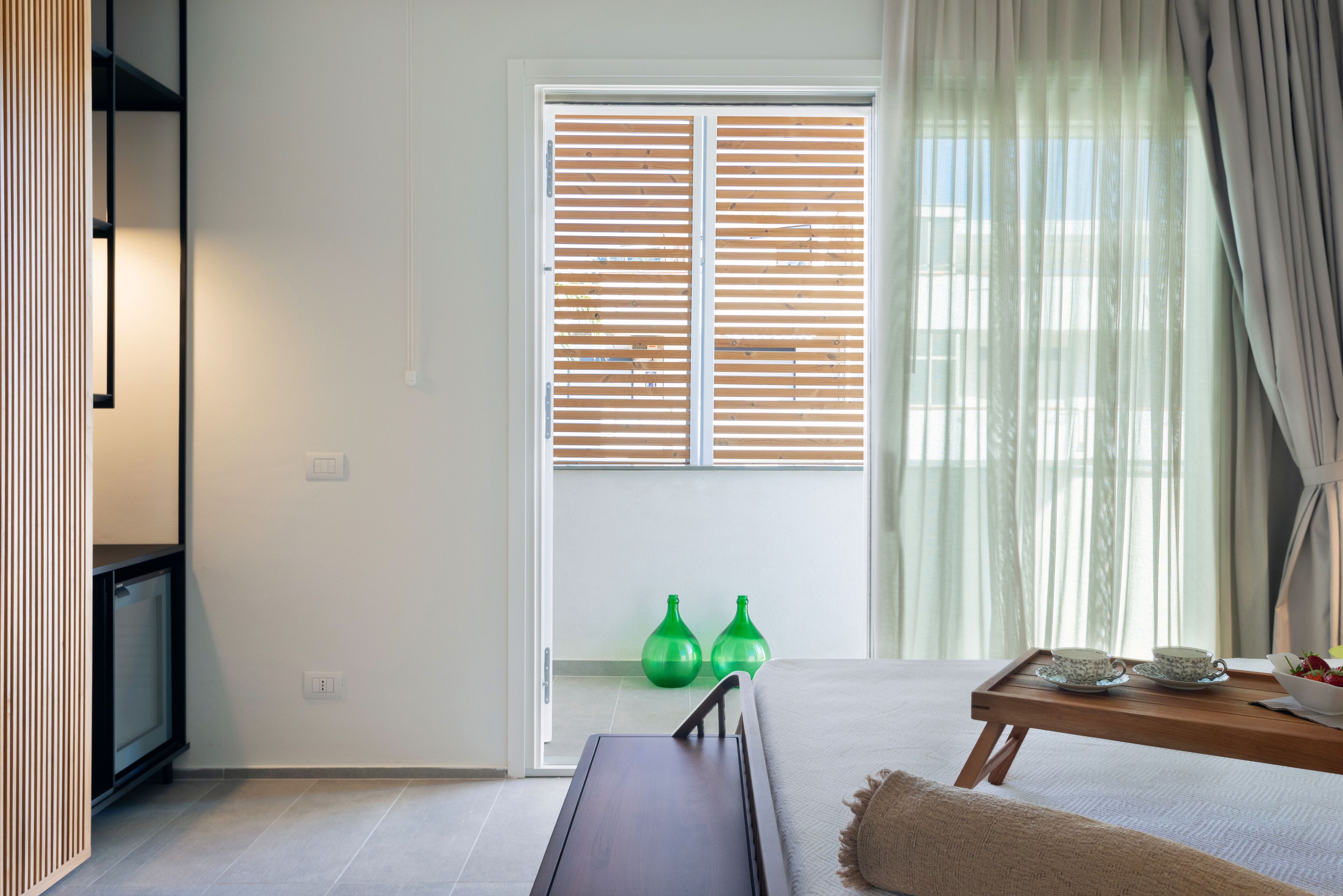 Une chambre d’hôtel moderne, avec un lit, une table de chevet en bois, une petite table avec un plateau, et un vase vert.