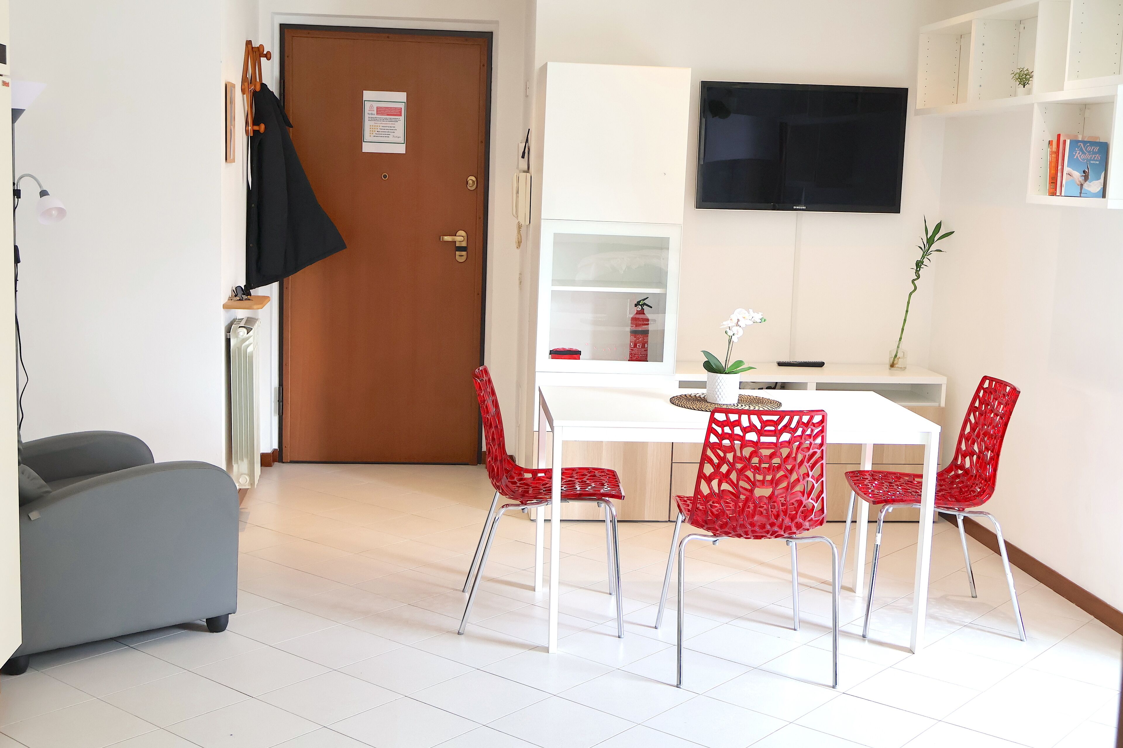 Ein modernes Zimmer mit einem weißen Tisch, roten Stühlen, einem grauen Sofa und einem wandmontierten Fernseher.