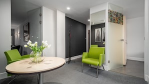 Une pièce moderne avec une table ronde, deux chaises vertes, un vase avec des fleurs blanches et un mur noir et blanc orné de deux tableaux encadrés.