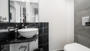 A modern bathroom with a white sink, black marble countertop, and a large mirror.