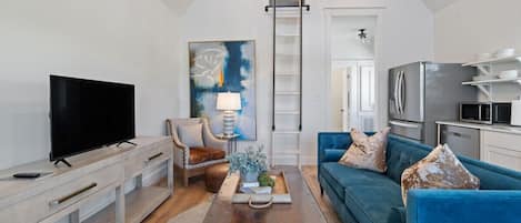 Un salon moderne avec un téléviseur à écran plat, un canapé bleu, une table basse et un tableau accroché au mur.