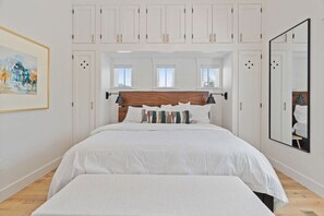Quarto com cama grande, cortinas brancas e espelho na parede.