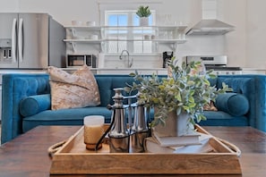 A modern kitchen with white appliances, a blue sofa, and a wooden coffee table with a tray.