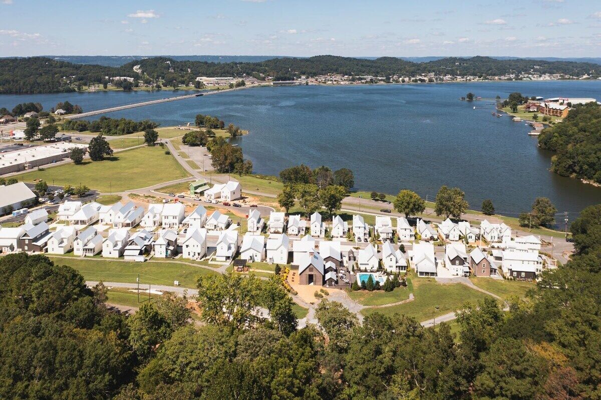 Un camping frente al lago con numerosas cabañas blancas y una amplia extensión de agua.