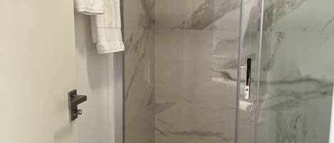 A glass-enclosed shower with a marble wall, a white toilet, and a towel hanging on the wall.