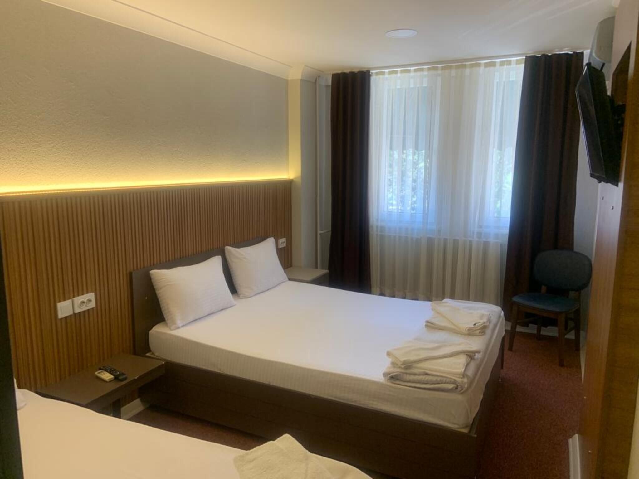 Une chambre d’hôtel comprenant un lit, une table de chevet, une chaise, une fenêtre avec des rideaux et un téléviseur fixé au mur.