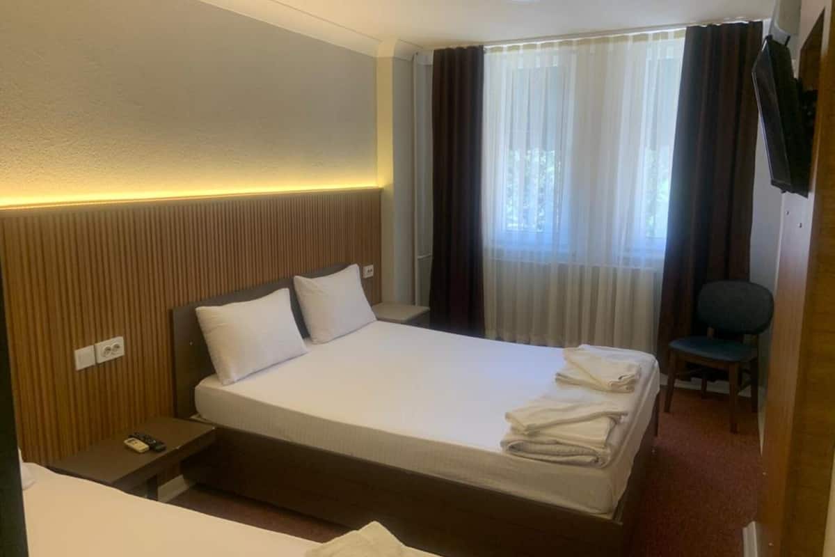 Une chambre d’hôtel comprenant un lit, une table de chevet, une chaise, une fenêtre avec des rideaux et un téléviseur fixé au mur.