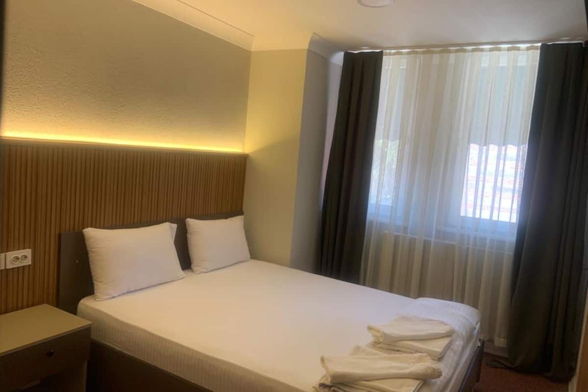Une chambre d’hôtel avec un lit, une table de chevet et une fenêtre avec des rideaux.