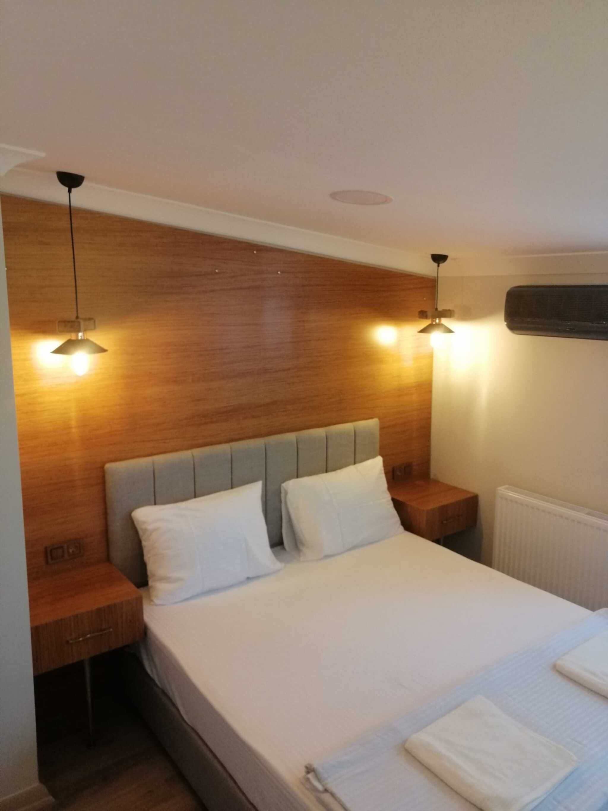 Une chambre à coucher comprenant un lit, deux tables de chevet, une tête de lit en bois et deux lampes suspendues.