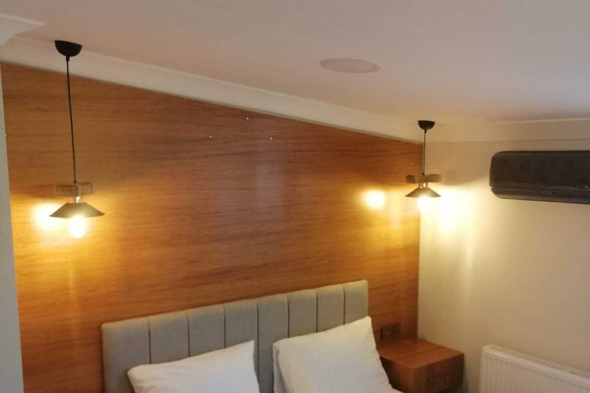 Une chambre à coucher comprenant un lit, deux tables de chevet, une tête de lit en bois et deux lampes suspendues.
