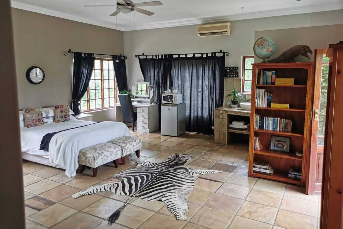 Ein Schlafzimmer mit Bett, Schreibtisch, Bücherregal, einem Zebra-Teppich und einem Deckenventilator.