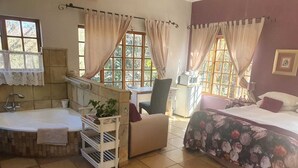 A room with a bathtub, a desk, a chair, a bed, and a window with curtains. - Deo Volente Country Estate  (Thabazimbi)
