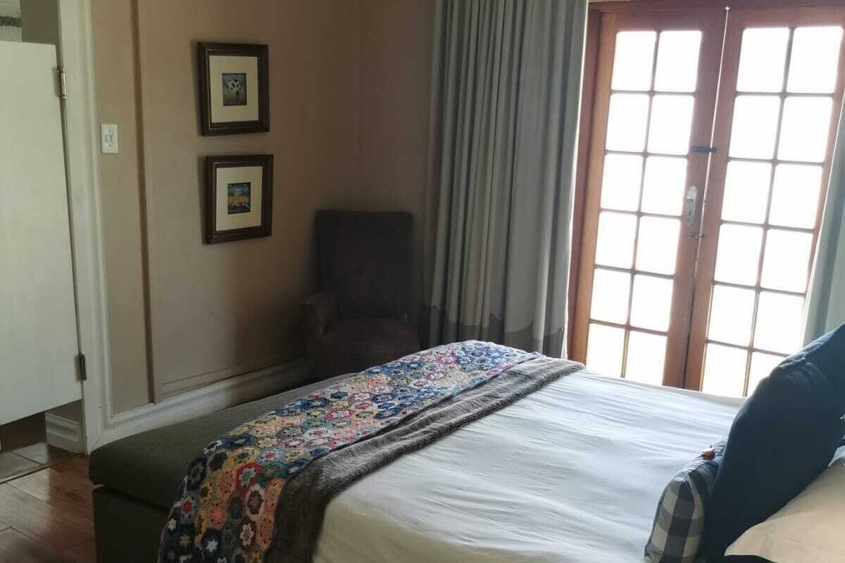 Ein Schlafzimmer mit einem Bett, einem Sessel, einem Fenster mit Vorhängen und zwei gerahmten Bildern an der Wand.