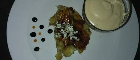Un plato blanco con un postre, un pequeño recipiente con salsa y algunos puntos negros y amarillos sobre un fondo oscuro.