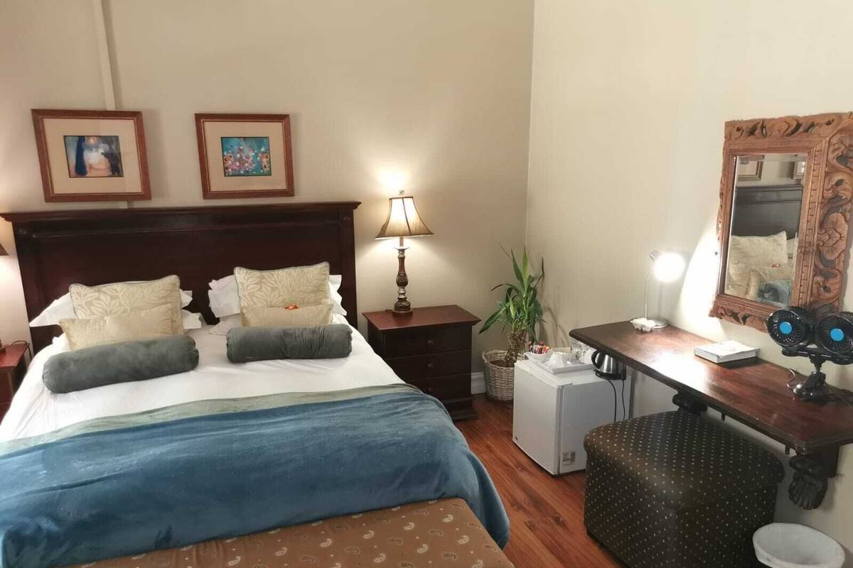 Ein Hotelzimmer mit einem großen Bett, einem Schreibtisch mit Computer, einem Spiegel und zwei gerahmten Bildern an der Wand.