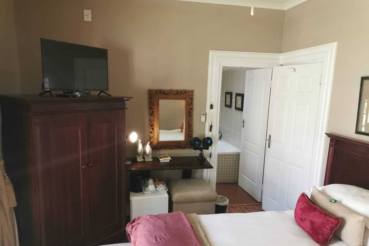 Ein Hotelzimmer mit Bett, Kommode, Fernseher, Spiegel und einem durchgehenden Tür erkennbaren Badezimmer.
