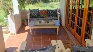 A covered patio area with a wooden bench, a cushioned sofa, and a dining table. - Deo Volente Country Estate  (Thabazimbi)