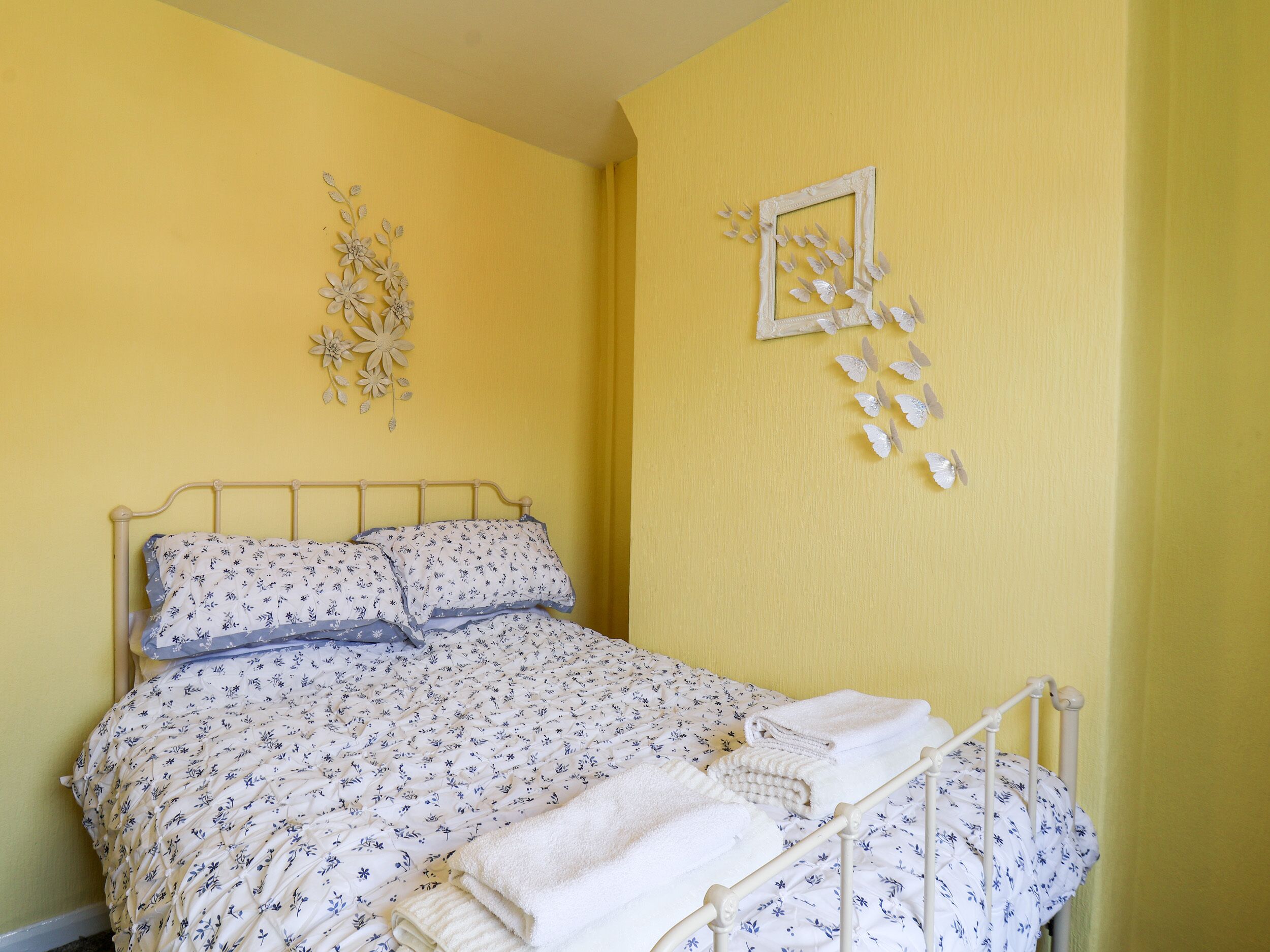 Een bed met bloemenbedekking, een wit metalen frame en decoratieve wandkunst.