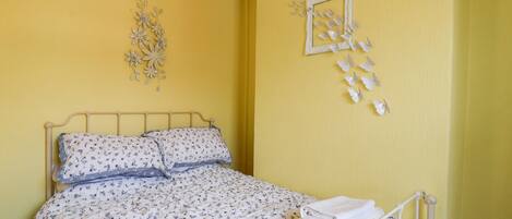Een bed met bloemenbedekking, een wit metalen frame en decoratieve wandkunst.