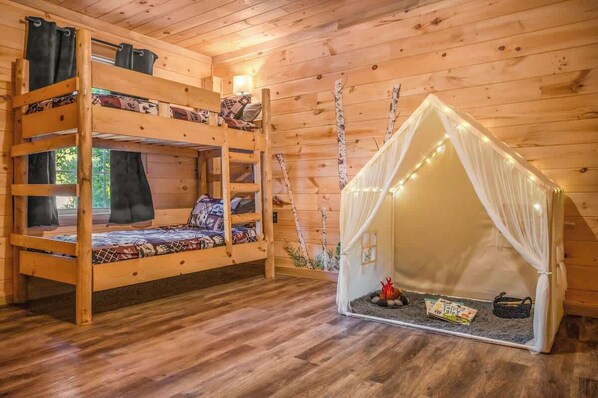 Una cabaña de madera con literas y una pequeña estructura parecida a una tienda de campaña con luces.