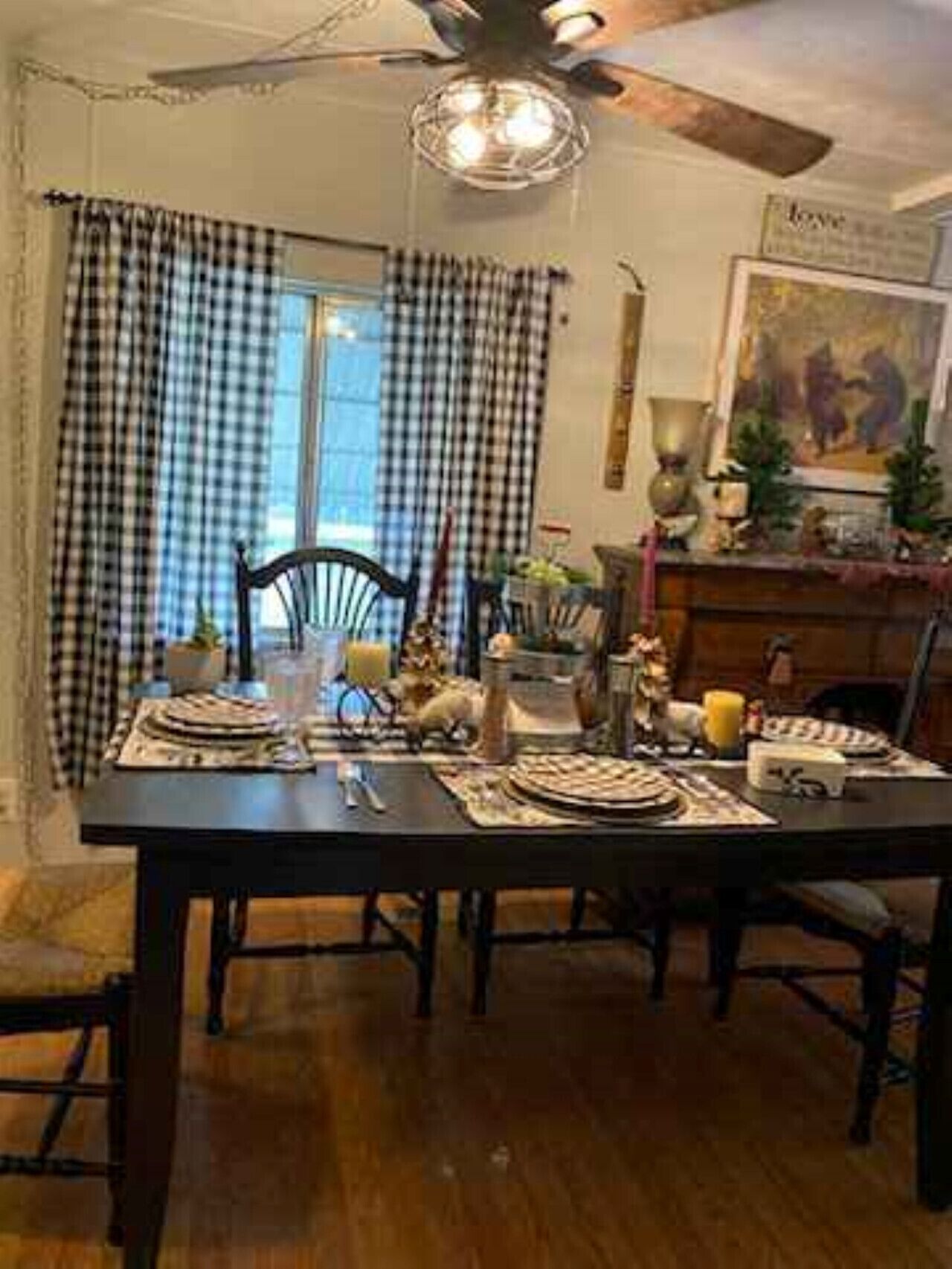 A dining area with a dark wooden table, checkered curtains, and a ceiling fan.