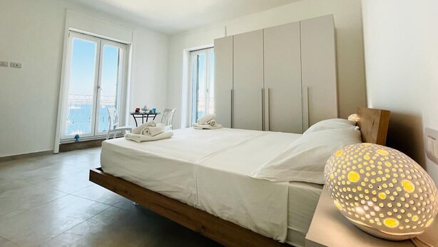 A modern bedroom with a bed, a bedside table, a lamp, and a view of the outside. - Dimora San Felice - I limoni (Gallipoli)