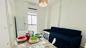 A compact living space with a dining table set for four, a dark blue sofa, and a white chair. - Dimora San Felice - I limoni (Gallipoli)