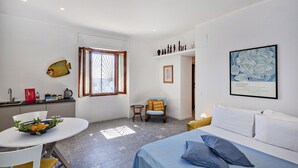 A modern hotel room with a bed, a dining table with a bowl of fruit, a chair, a window with curtains, and a framed artwork on the wall. - Yellow Suite a Recco by Wonderful Italy (Recco)
