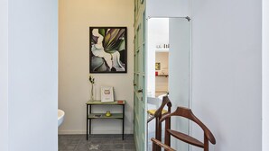 A narrow hallway with a door leading to a bathroom. A framed picture hangs on the wall, and a small table with a vase and a book is placed against the wall. - Yellow Suite a Recco by Wonderful Italy (Recco)