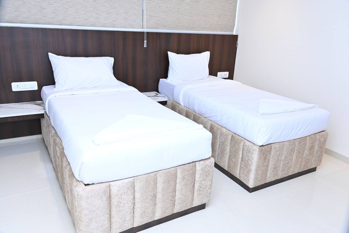 Two single beds with white linens in a modern room with a wooden headboard and a white floor.