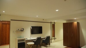 Een moderne hotelkamer met een bureau, twee stoelen, een televisie, een kledingkast en een kleine tafel met een stoel.