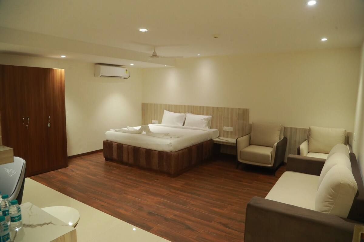 A hotel room with a bed, a sofa, a chair, a desk, and a wardrobe.
