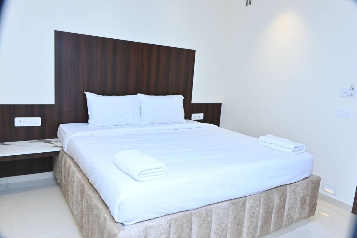 A neatly made bed with white linens and pillows, a wooden headboard, and a bedside table with a lamp.
