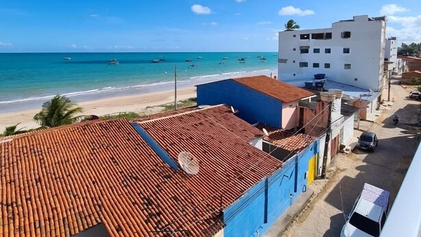 Vista costera con una playa, un edificio blanco con techo rojo y un edificio azul.