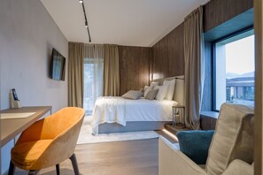 A modern hotel room with a bed, a desk, a chair, and a large window offering a view. - Collina Luxury Relais  (Clusone)