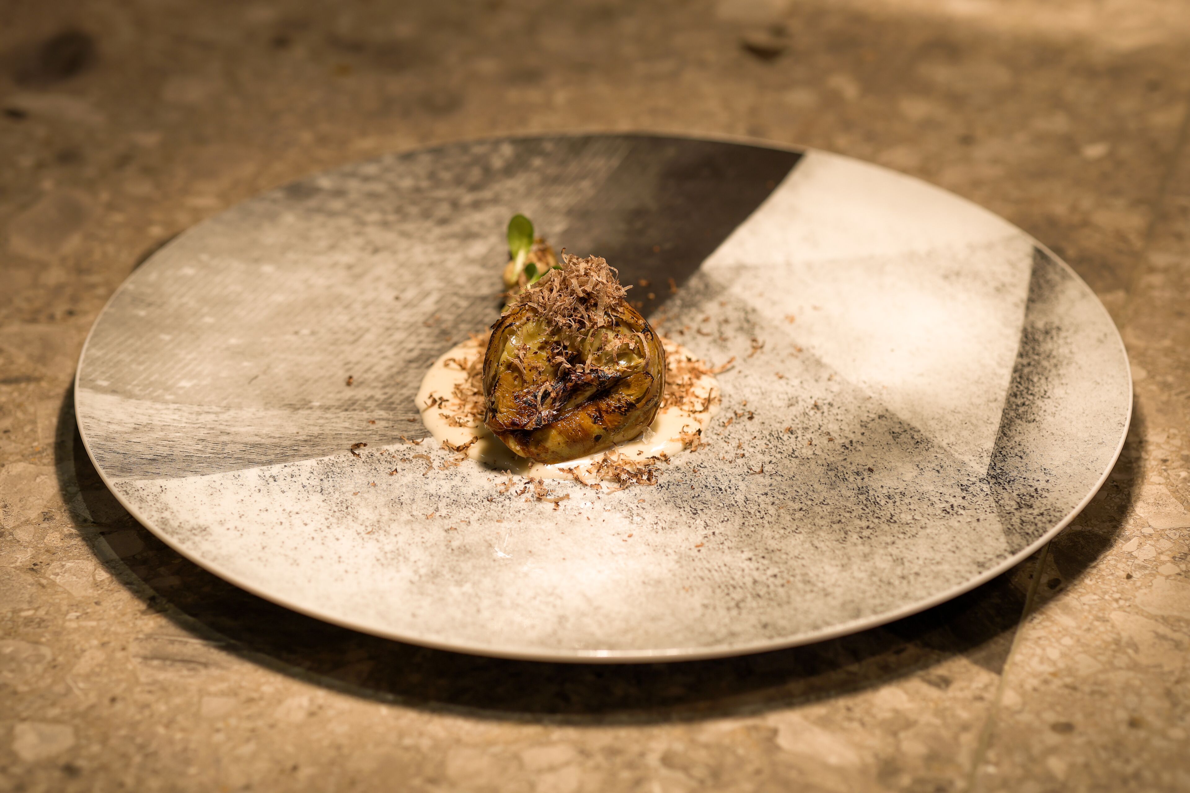 A plate with a single food item, possibly a stuffed vegetable, on a textured surface.