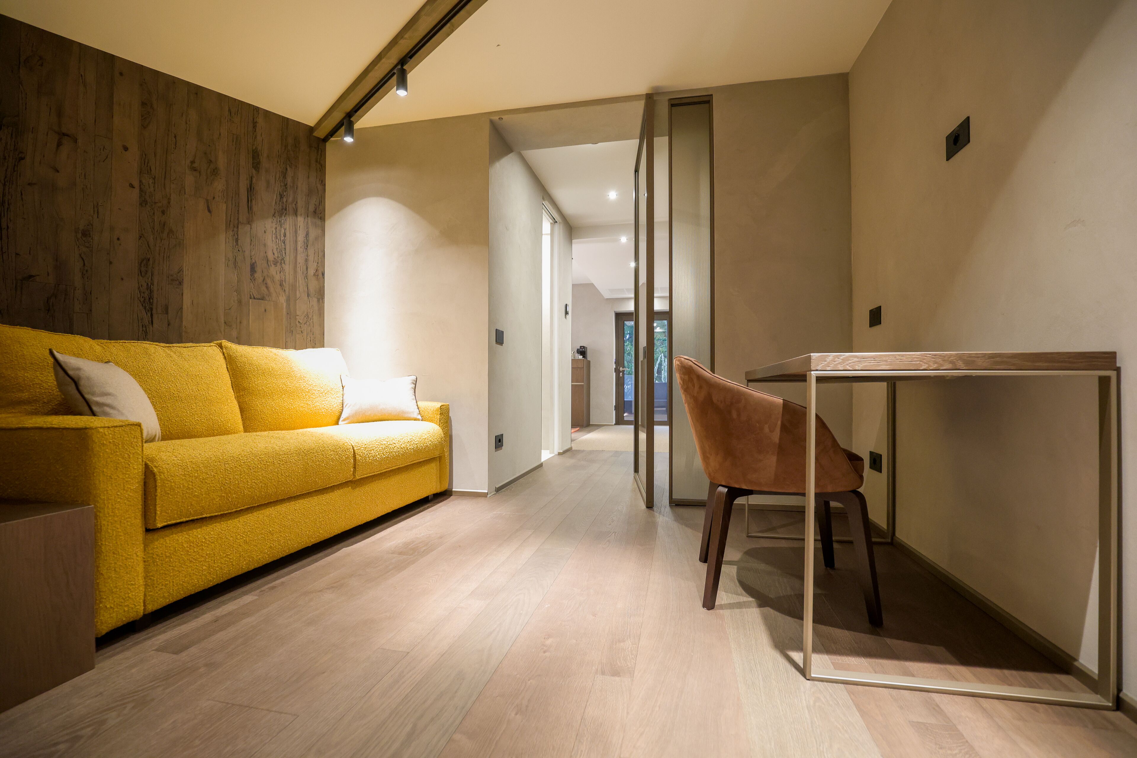 A modern living room with a yellow sofa, a wooden accent wall, and a dining area with a glass table and chair.