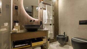 Un baño moderno con un mueble de tocador de madera, un espejo grande, un lavabo negro, un inodoro y un perchero para toallas.