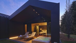 A modern house with a hot tub, lounge chairs, and a well-lit interior. - Collina Luxury Relais  (Clusone)