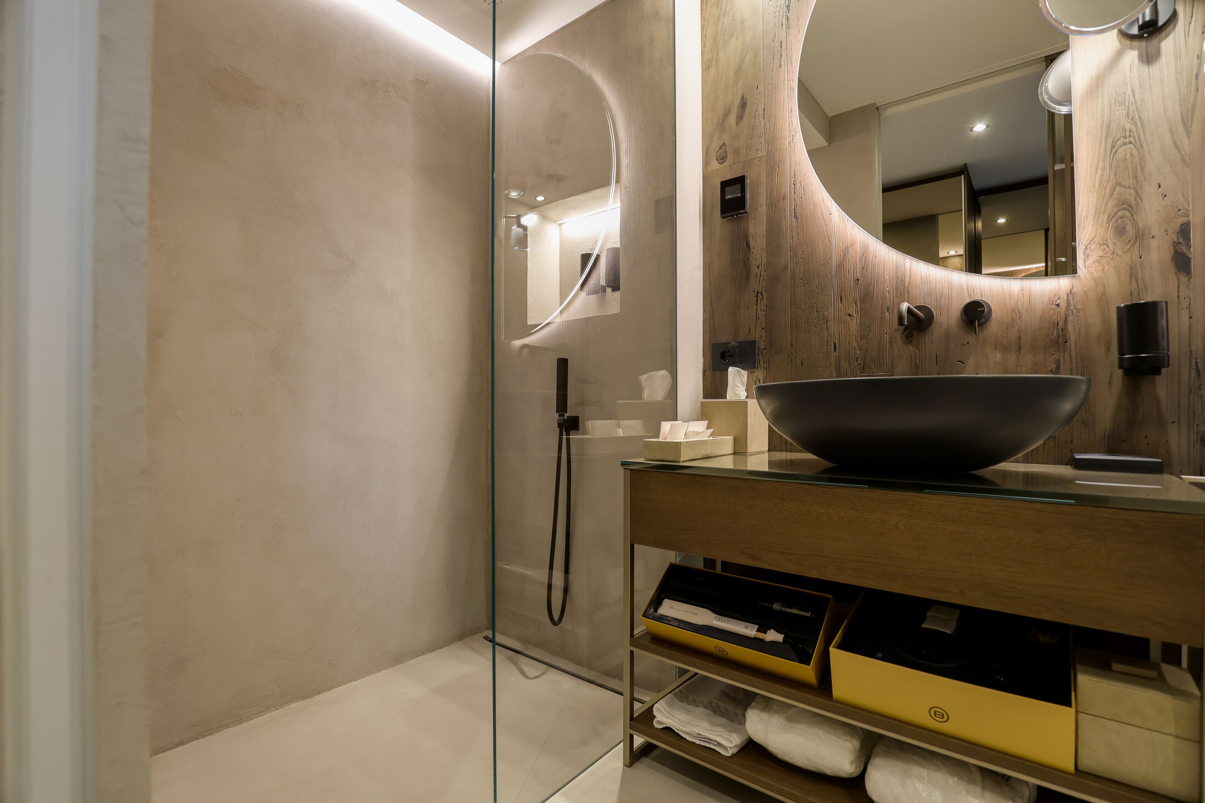 A modern bathroom with a glass shower enclosure, a wooden vanity with a large bowl sink, and a mirror with a wooden frame.