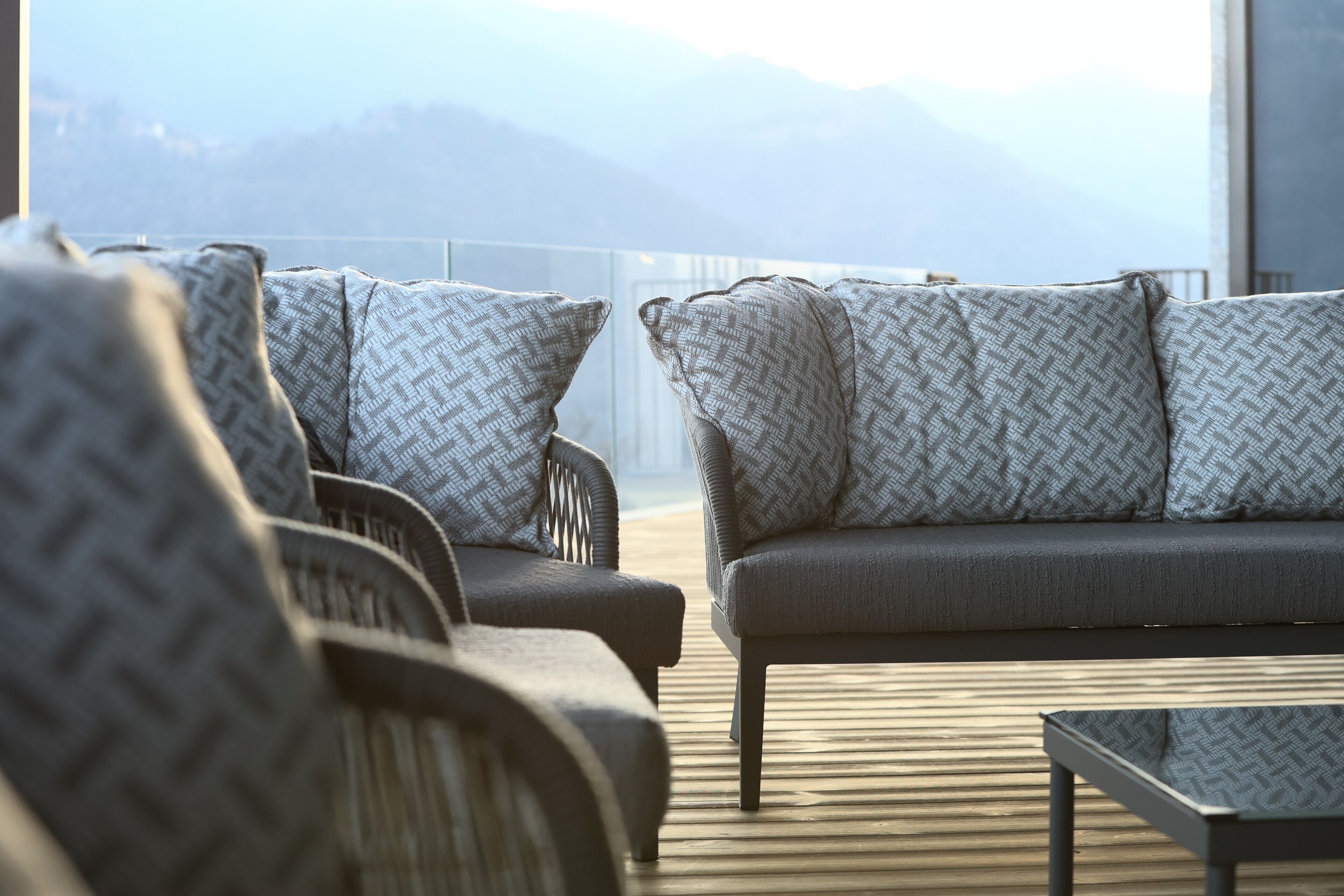 A modern outdoor seating area with patterned cushions and a wooden deck, overlooking a mountainous landscape.