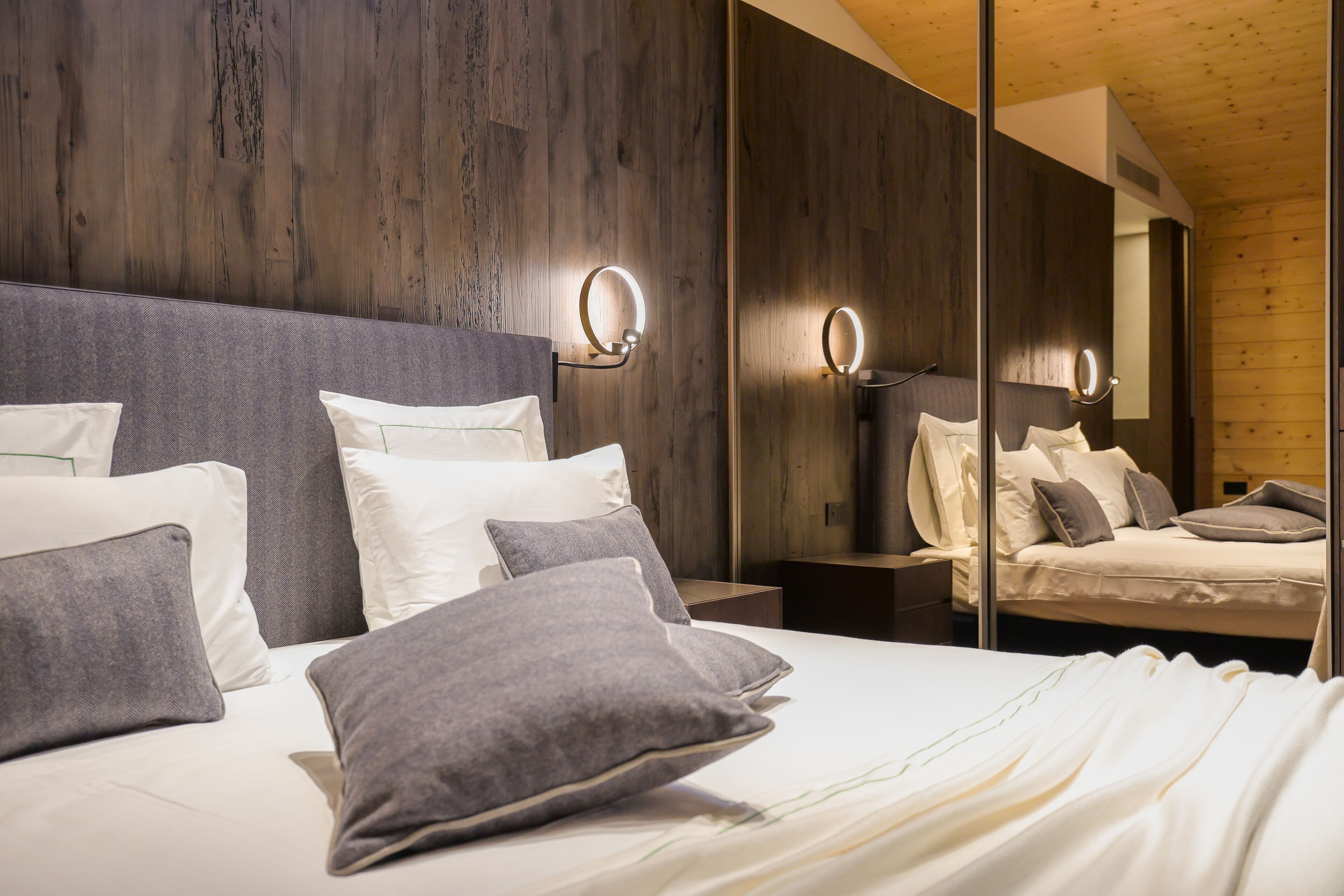 Un dormitorio moderno con una cama grande, ropa de cama gris y blanca, y luces empotradas en la pared.