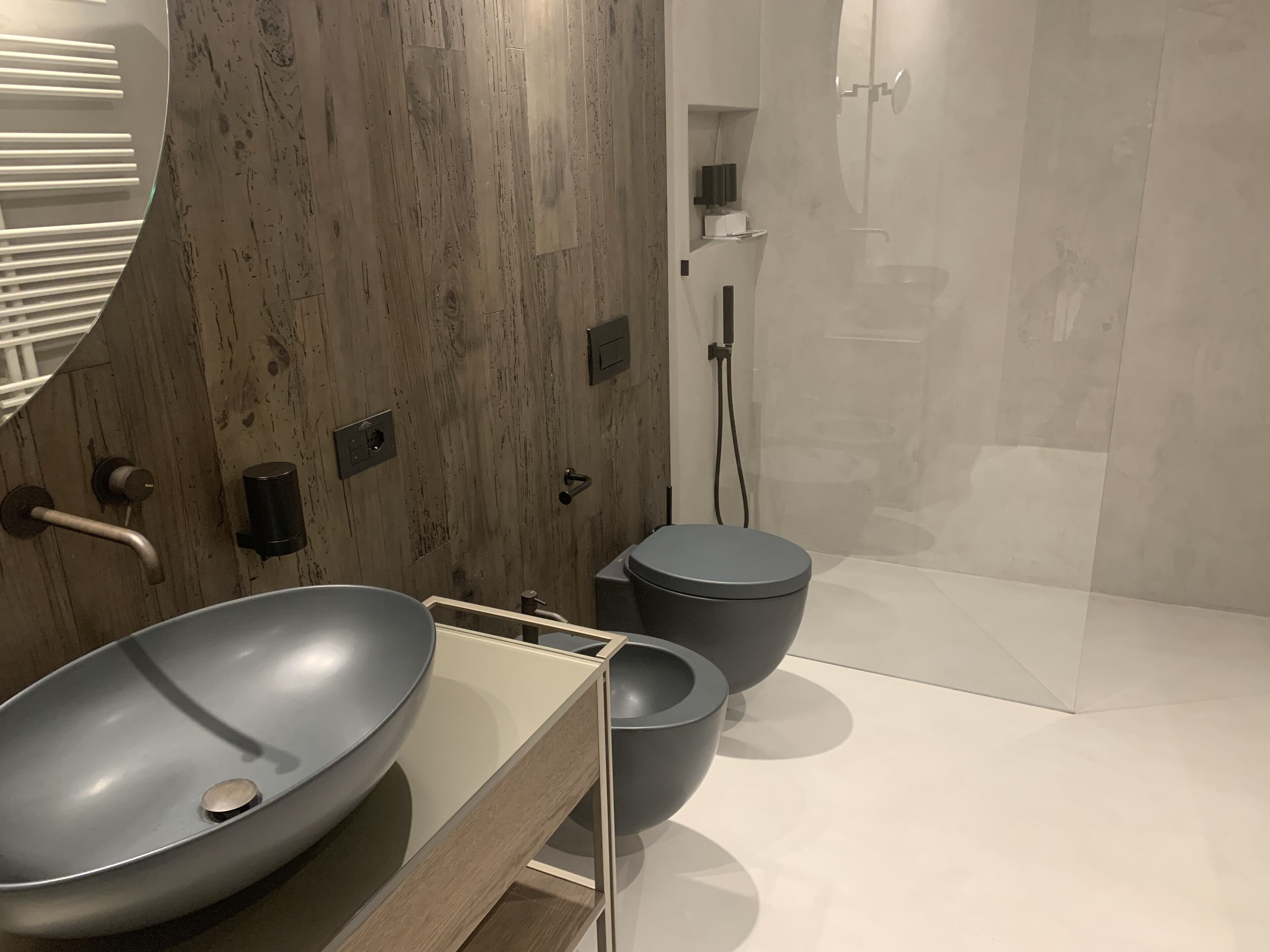 Un baño moderno con tocador de madera, un lavamanos grande tipo recipiente y un inodoro separado.