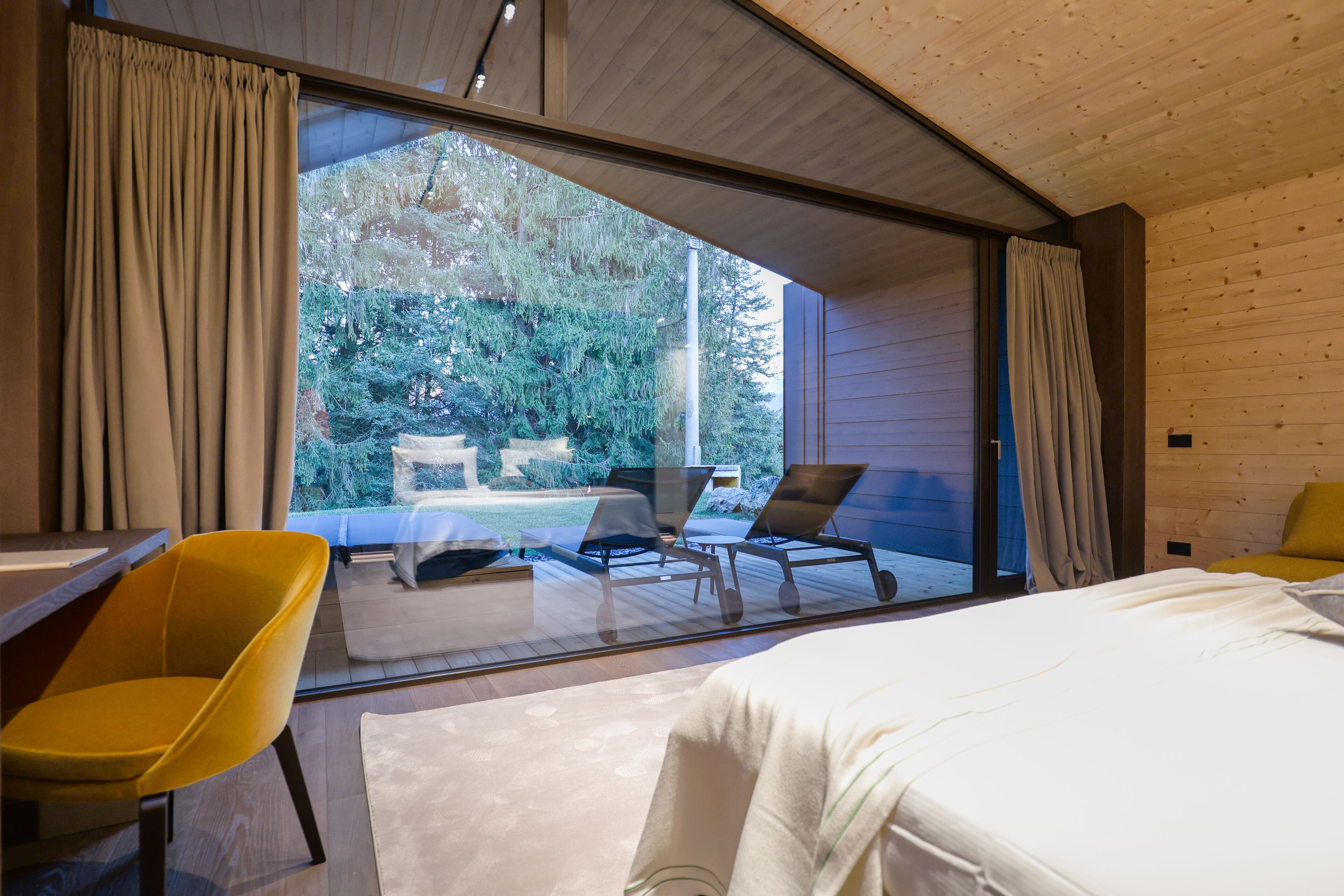 A modern bedroom with a large sliding glass door leading to a balcony. The room features a bed, a yellow chair, and a small table.