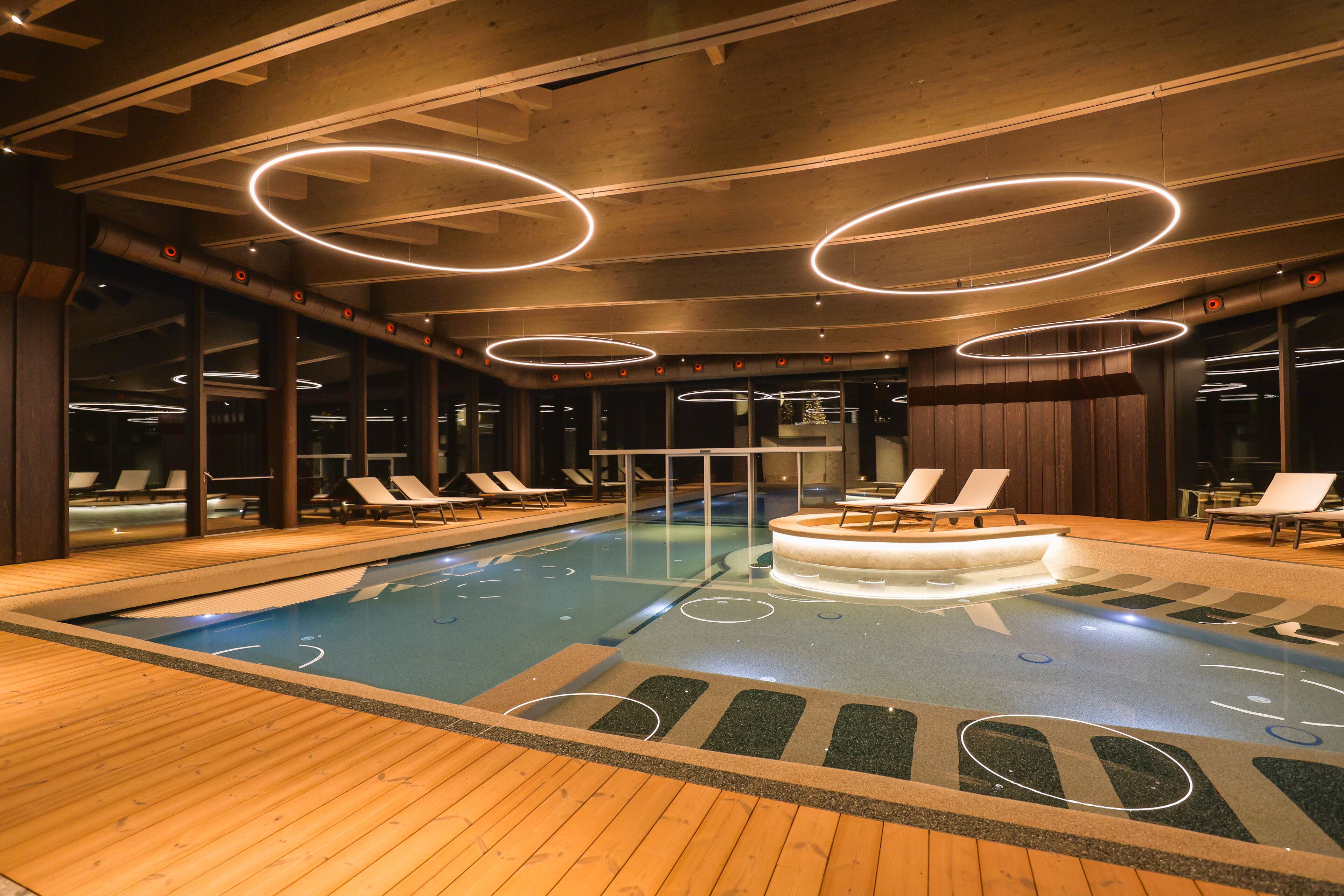 An indoor swimming pool with wooden flooring and lounge chairs.