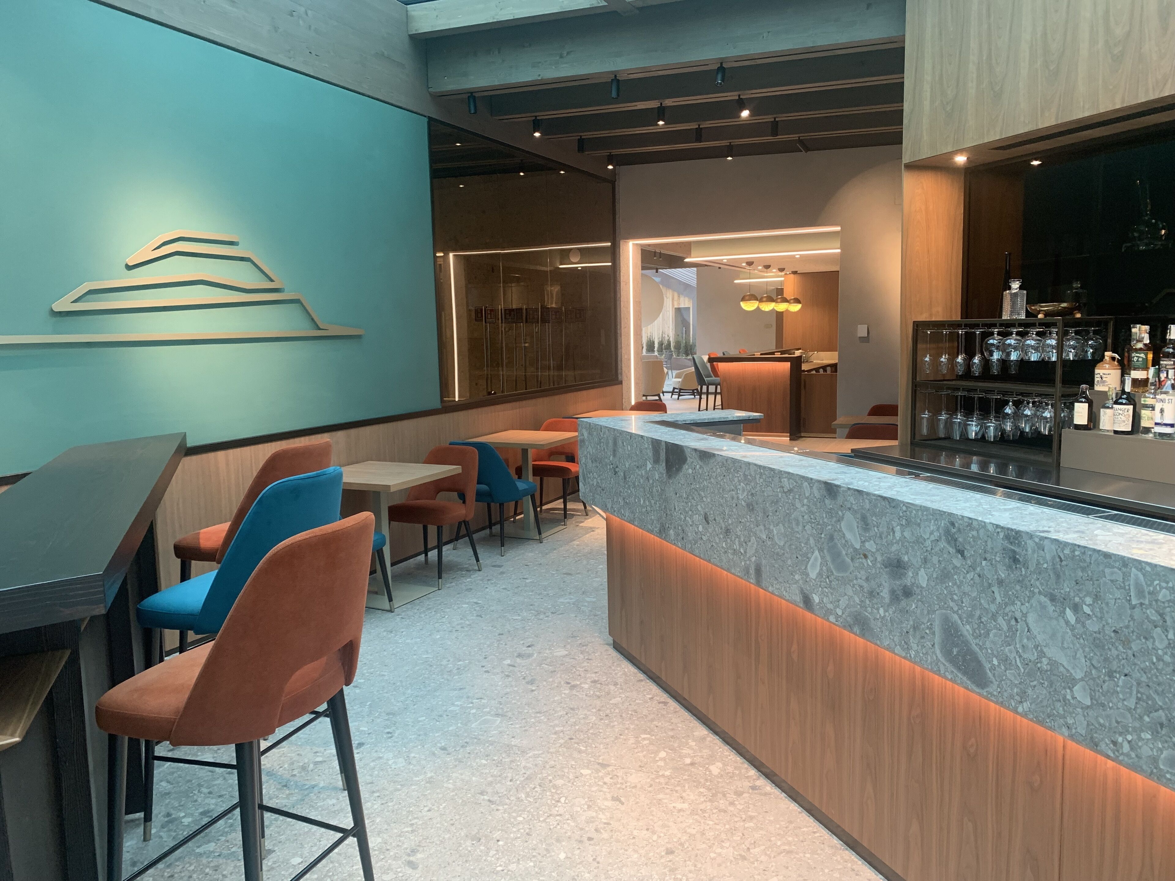 Eine moderne Bar mit einer Marmor-Bar, Sitzgelegenheiten mit orangefarbenen und blauen Stühlen, und einer gut sortierten Bar mit Gläsern und Flaschen.