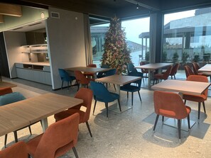A modern dining area with tables and chairs, a Christmas tree, and a view of a building through large windows. - Collina Luxury Relais  (Clusone)